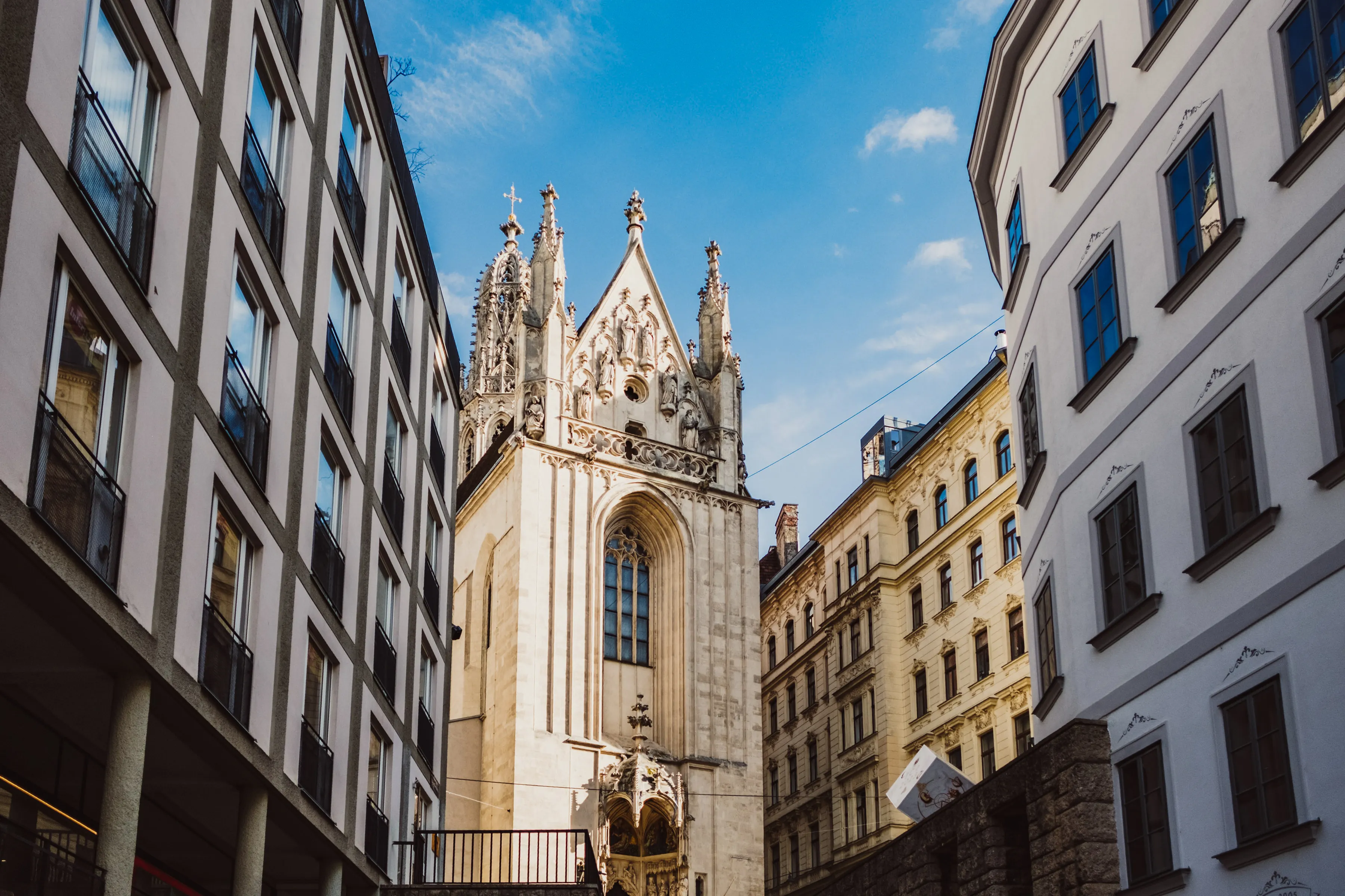 Blick durch eine Gasse zwischen Altbaufassaden auf die gotische Kirche Maria am Gestade